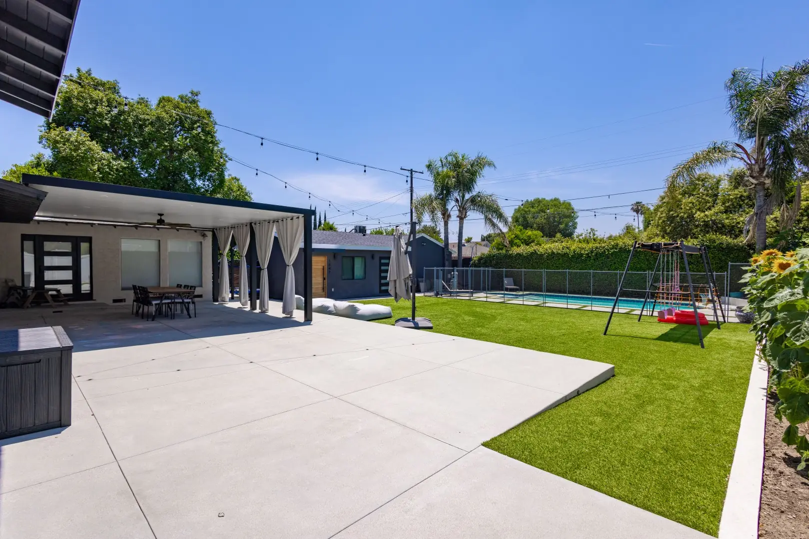 Dark-framed pergola with white curtains over a patio beside a turf lawn in Reseda, Los Angeles